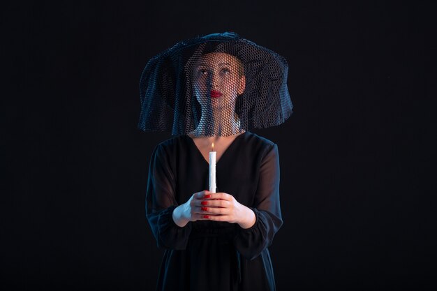 Mournful female dressed in black holding candle on black  death funeral sadness