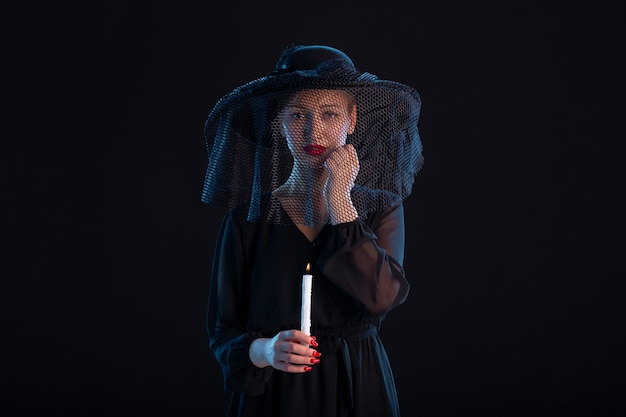 Mournful female dressed in black with burning candle on black  sadness funeral death