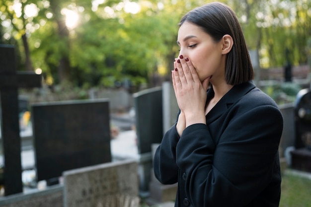 Free photo mourning woman praying next to grave at the cemetery