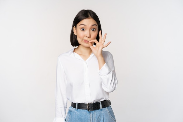 Mouth shut Young asian woman seal lips showing taboo dont speak keep quiet sign hiding secret standing over white background