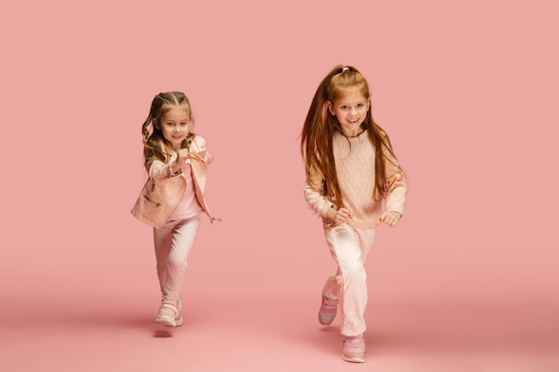 Foto gratuita mossa. bambini felici, ragazze isolate su sfondo rosa corallo per studio. sembra felice, allegro. copyspace per l'annuncio. infanzia, educazione, emozioni, concetto di espressione facciale. saltare, correre divertendosi