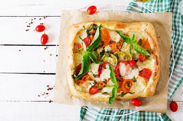 Mozzarella, tomatoes, basil savory pie on a white wooden table. Delicious food, appetizer in a mediterranean style. Top view. Flat lay