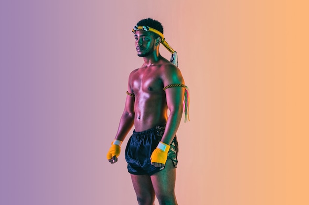 Muay thai. Young man exercising thai boxing on gradient background in neon light.