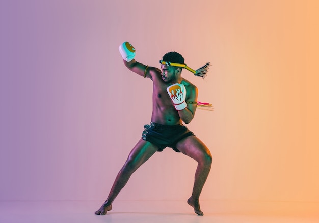 Muay thai. Young man exercising thai boxing on gradient background in neon light.