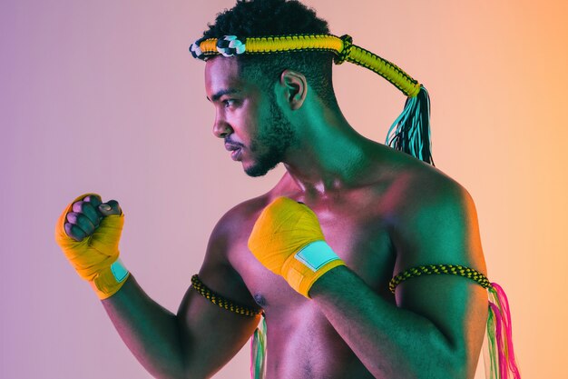 Muay thai. Young man exercising thai boxing on gradient background in neon light.