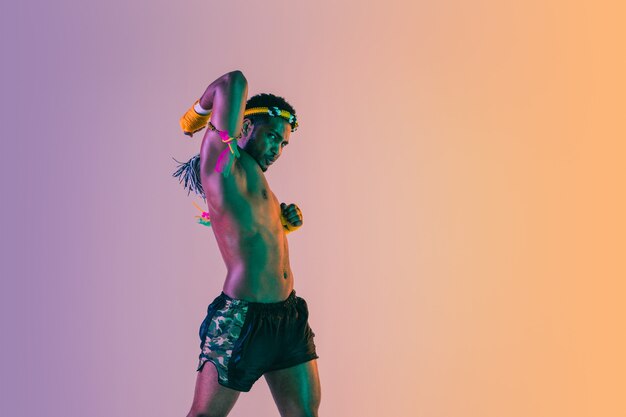 Muay thai. Young man exercising thai boxing on gradient background in neon light.