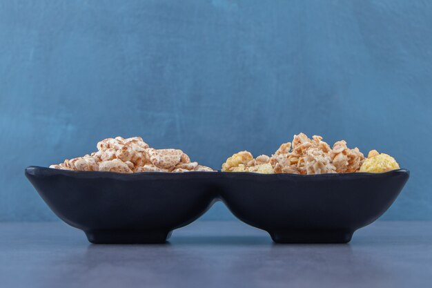 Muesli and cornflakes in bowls, on the marble background.