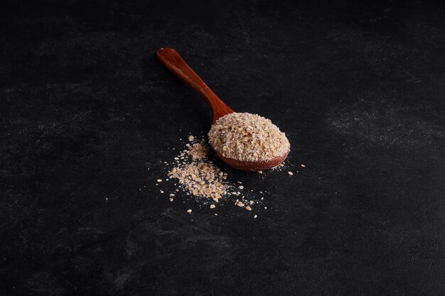 Mueslies in wooden spoon on black surface. 