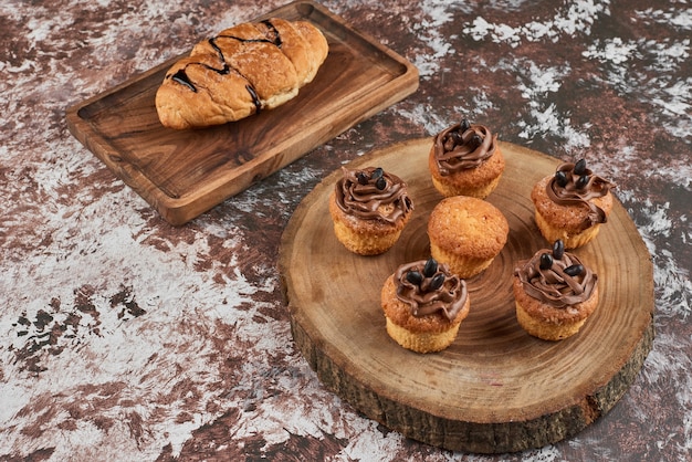 Muffins and croissant on a wooden board.