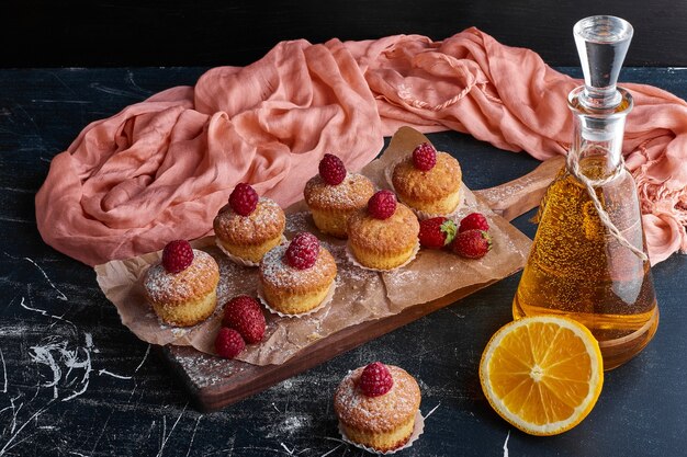 Muffins with raspberries on wooden board. 
