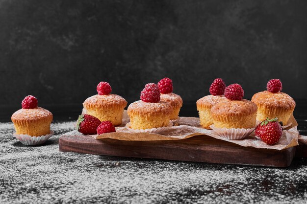 Muffins with raspberry on wooden platter.