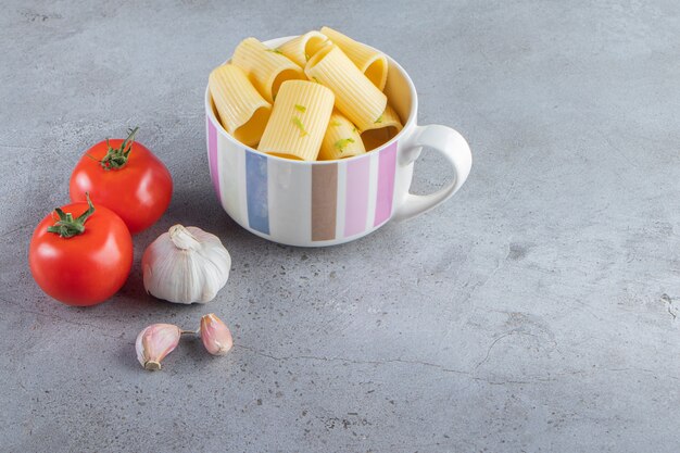 Mug of boiled calamarata pasta with vegetables on stone background. 