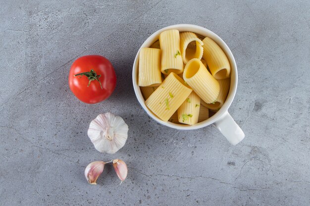 Mug of boiled calamarata pasta with vegetables on stone surface.