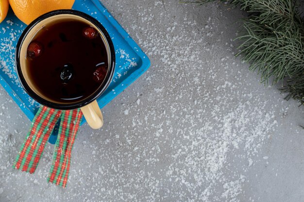 Mug of dog rose tea on a platter with oranges in a festive setup on marble surface