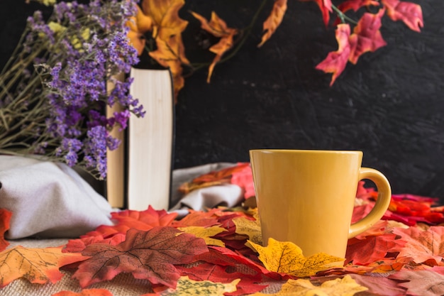 Mug on leaves near books and flowers