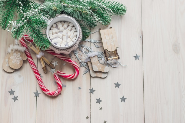 Mug of marshmallows and candy canes surrounded by Christmas decorations on the table