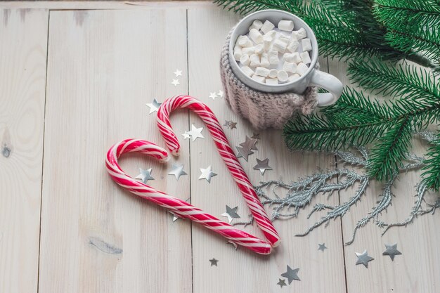 木製のテーブルの上のクリスマスの装飾に囲まれたマシュマロとキャンディケインのマグカップ