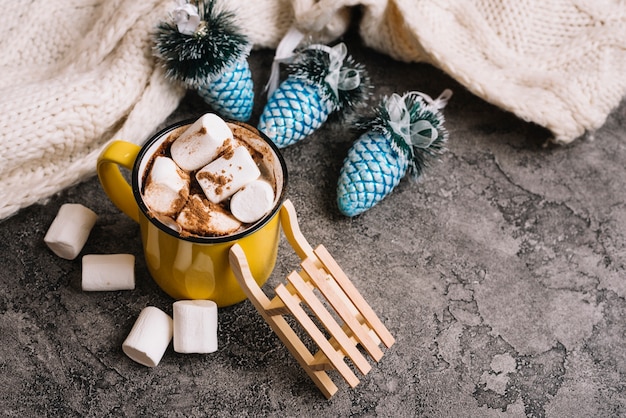 Mug with marshmallows near Christmas toys and sweater