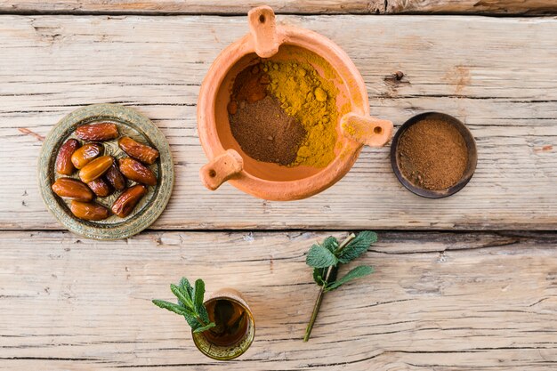 Mug with plant twig near dried fruits and spices in bowl