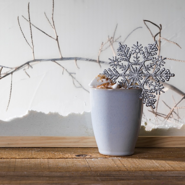 Mug with toy snowflake on wood table near bank of snow