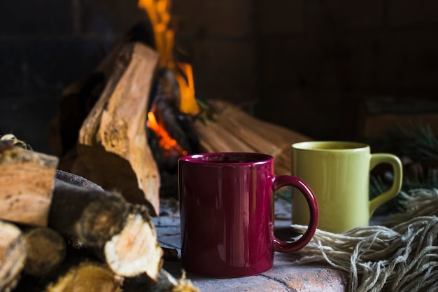 Mugs and blanket near fire in fireplace