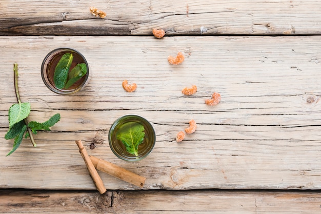 Mugs of drink near cinnamon, plants and nuts on board