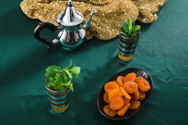 Mugs of drink near silver teapot and dried apricots