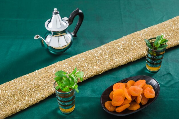 Mugs of drink near teapot and dried apricots 