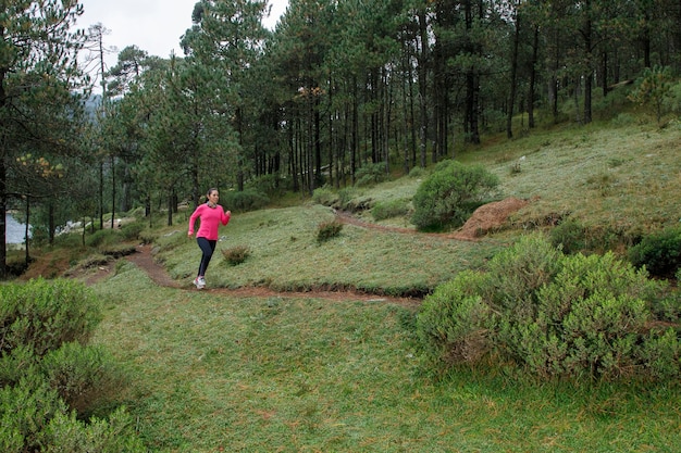 Mujer corriendo en un sendero del bosque con arboles al fondo