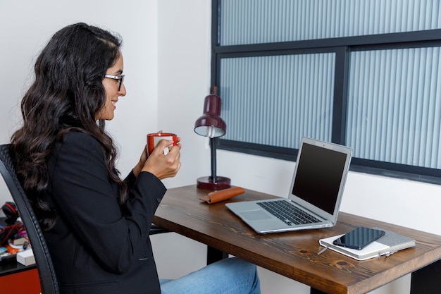 Mujer ejecutiva tomando una taza de cafe mientras esta en conferencia en su ordenador portatil