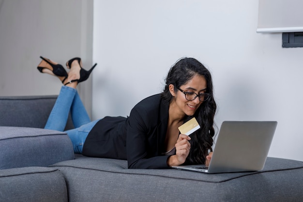 Mujer latina haciendo compras en su computadora portatil y pagando con tarjeta de credito desde casa Premium写真