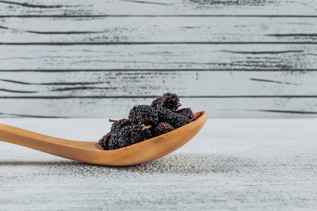 Mulberries in a wooden spoon side view on a light wooden background free space for your text