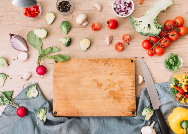 Multi colored vegetables surrounded near the wooden chopping board