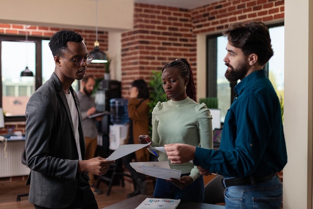 Multi-ethnic businesspeople discussing business collaboration after analyzing marketing statistics. Freelancer woman explaining company strategy working at financial project in brick wall office