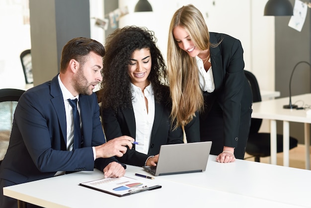 現代的なオフィスで3人のビジネスマンを集めた多民族グループ。 2人の女性とラップトップコンピュータを見ているスーツを着ている白人男性。
