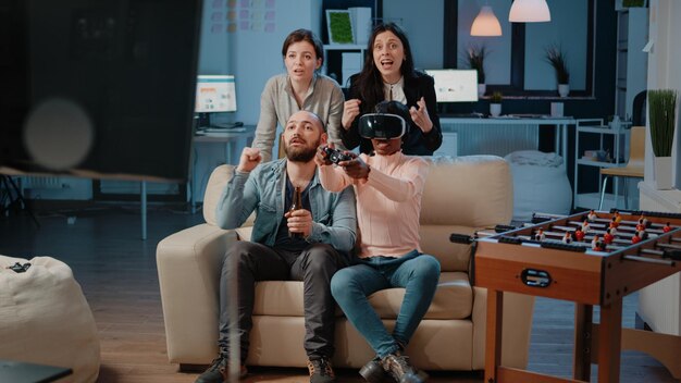 Multi ethnic people cheering while woman winning game with vr
glasses and controller on tv console. workmates enjoying video
games with joystick to have fun with activity after work