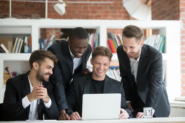 Multi-ethnic smiling businessmen in suits watching something funny on laptop 