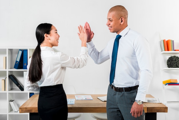 Multi ethnic young businessman and businesswoman giving high-five to each other at workplace