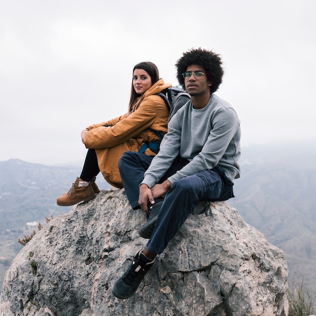 멀티 민족 젊은 부부는 카메라를보고 바위 꼭대기에 앉아