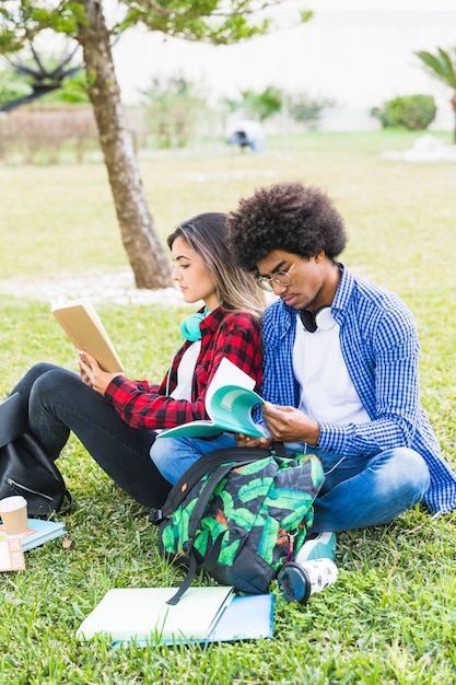 Multi ethnic young couple students sitting on campus reading the books together