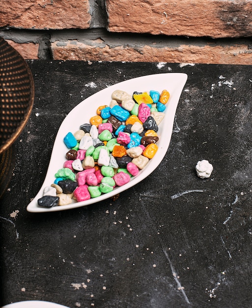 Dolci multicolore del bonbon (caramelle della palla) dentro la ciotola del piatto bianco sul mattone di pietra