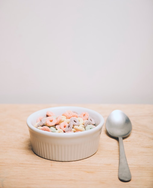 Multicolor cereals in the white bowl and spoon on wooden desk against white background