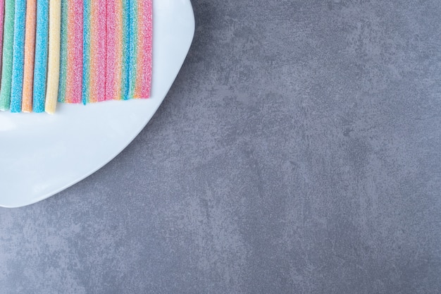 Multicolor gummy candy sweets on a plate on marble table.