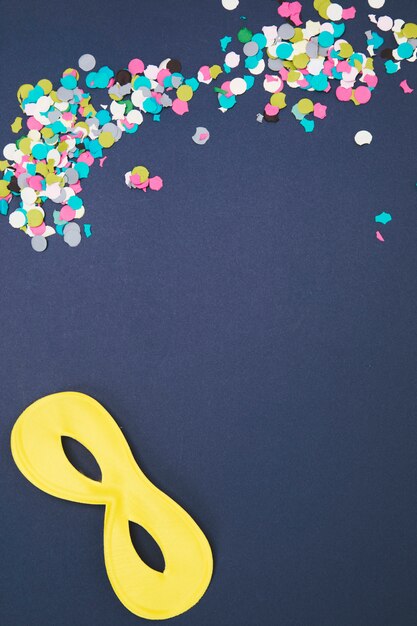 Multicolored confetti with yellow eye mask on colored background