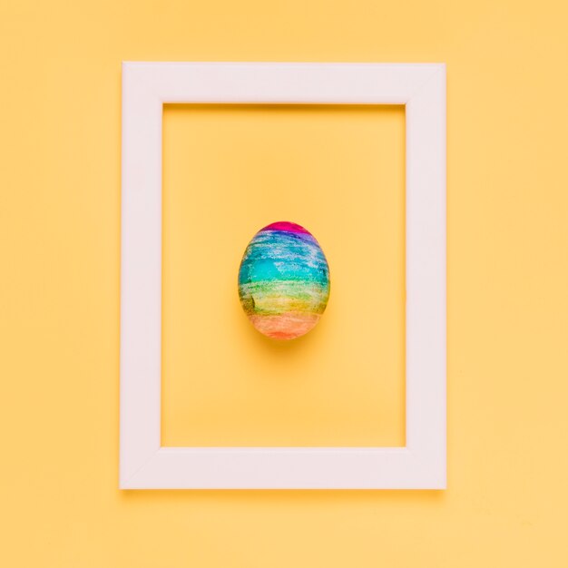 Multicolored easter egg inside the white border frame on yellow backdrop