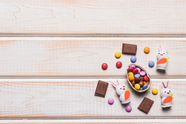 Multicolored gem candies on egg shell; gems; bunnies and chocolate pieces on wooden surface