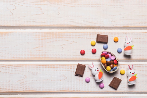 Разноцветные драгоценные конфеты на яичной скорлупе; драгоценные камни; кролики и кусочки шоколада на деревянной поверхности
