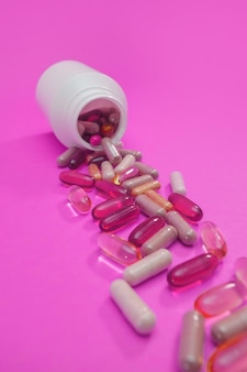 Разноцветные таблетки и капсулы на розовом фоне