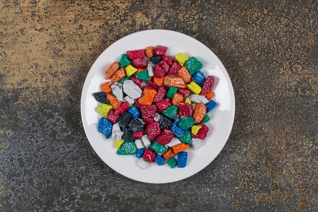 Multicolored stone candies on white plate.