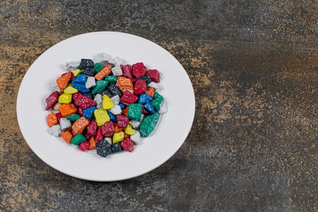 Multicolored stone candies on white plate.